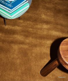 a stack of books sitting on top of a brown carpet next to a wooden table