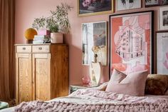 a bedroom with pink walls and pictures hanging on the wall above it, along with a bed in front of a dresser