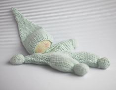 a green knitted stuffed animal laying on top of a white tablecloth covered surface