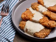 fried chicken covered in gravy on a plate with a fork and napkin next to it