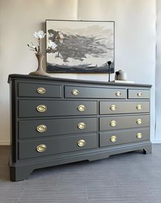 a large gray dresser with gold handles and knobs in a white walled room next to a painting on the wall