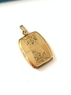 a gold pendant with an ornate design on the front and back of it, sitting on a white surface