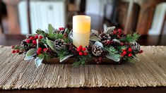 a candle sits on top of a wooden tray with holly and pine cones, surrounded by berries