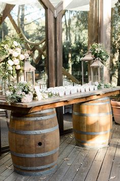 a wooden table topped with lots of vases filled with flowers next to two wine barrels