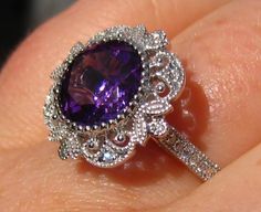 a close up of a person's hand holding a ring with a purple stone in it