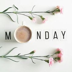 a cup of coffee sitting on top of a white table next to pink flowers and scrabbles