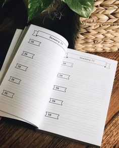 an open notebook sitting on top of a wooden table next to a potted plant