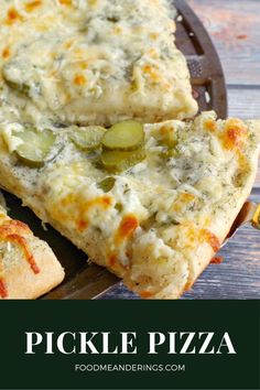 two pieces of pizza with cheese and pickles on them sitting on a wooden table