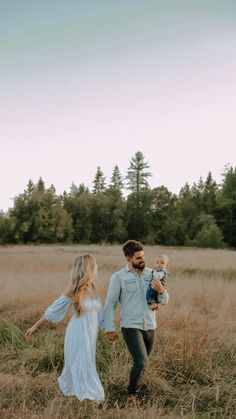 a man and woman walking through a field with a baby in their arms while holding hands