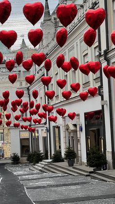 many red heart shaped balloons are floating in the air above a street lined with buildings