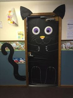 a door decorated to look like a black cat with purple eyes and tail, standing in front of a classroom wall