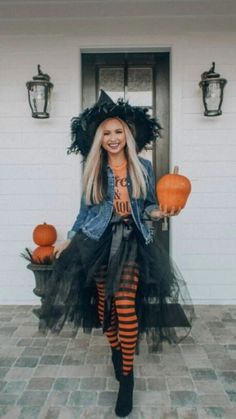 a woman dressed up as a witch standing in front of a house with pumpkins