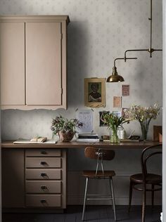 a desk with flowers and pictures on the wall next to a chair in front of it