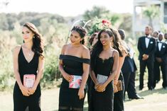 three women in black dresses standing next to each other at a formal event with people looking on