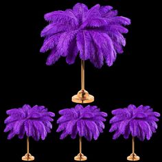 purple ostrich feathers are placed on gold pedestals in front of a black background