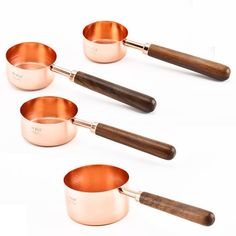 four copper pans with wooden handles are lined up