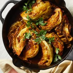 an iron skillet filled with cooked cabbages and parsley on top of a table