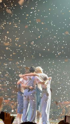 three people hugging each other on stage with confetti falling in the air