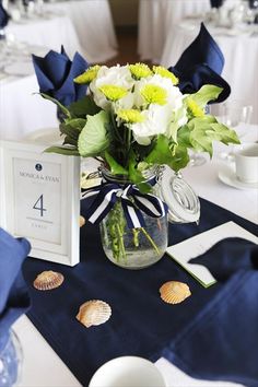 a vase filled with white and yellow flowers on top of a blue table cloth covered table