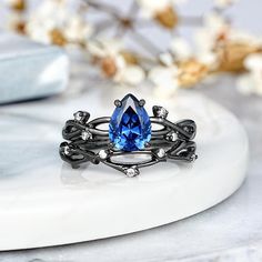 an image of a ring with a blue stone in it on a marble table next to flowers