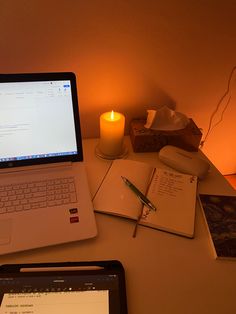 an open laptop computer sitting on top of a desk next to a notebook and candle