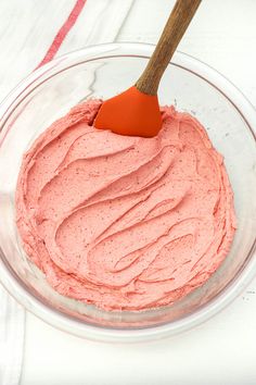 a bowl filled with pink frosting and a wooden spatula in it on top of a white table