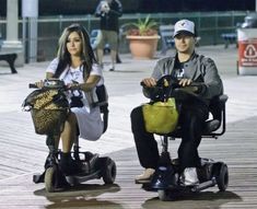 two people riding scooters on the street at night with one person sitting down