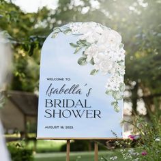 a welcome sign for a bridal shower with flowers on it in front of some trees