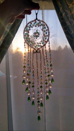 a hand holding a beaded dream catcher in front of a window