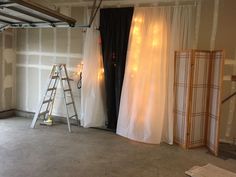 an empty room with white curtains and lights on the wall, next to a ladder