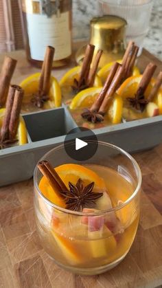 a glass filled with liquid sitting on top of a wooden table next to sliced oranges and cinnamon sticks