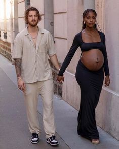 a pregnant woman walking down the street with a man holding her hand and looking at him