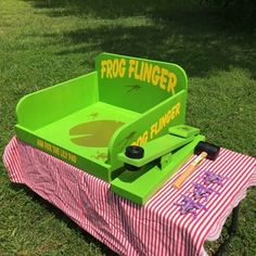 a green toy wagon sitting on top of a grass covered field next to a pink and white table cloth