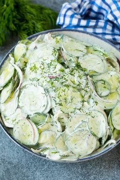 a bowl filled with cucumbers and dill on top of a table next to a blue checkered napkin