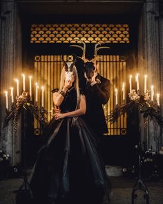 a man and woman dressed in black standing next to each other with candles behind them