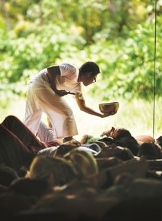 a man is holding a bowl in his hand while others are laying on the ground