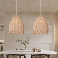 two lamps hanging over a white table in a room with chairs and a vase on it