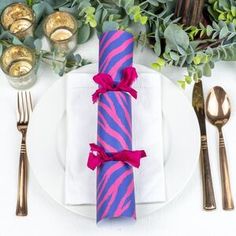 a place setting with pink and purple napkins, silverware, and gold cutlery