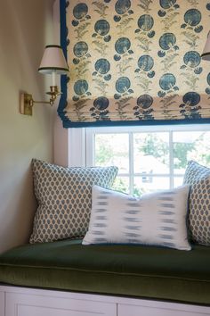 a window seat with pillows on it in front of a window sill and two lamps