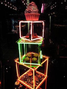 an illuminated display with cupcakes and other items in the center, all stacked on top of each other