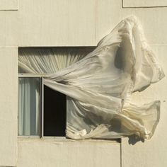 an open window covered in white fabric next to a curtain on the side of a building