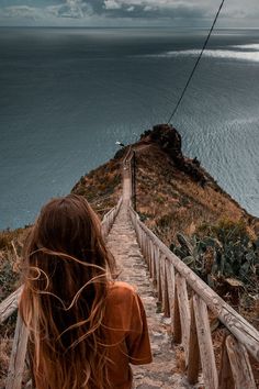 a woman is walking down the stairs towards the ocean on a cloudy day with her hair blowing in the wind