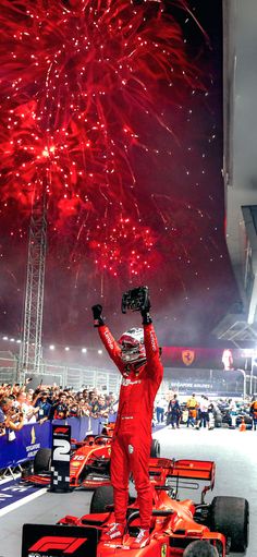 a man standing on top of a race car with fireworks in the sky behind him