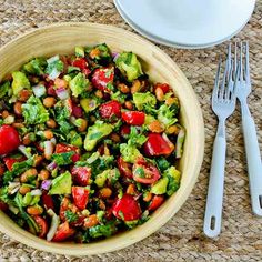 a wooden bowl filled with salad next to a fork and knife on top of a table