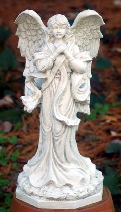 an angel statue sitting on top of a potted plant in front of some grass