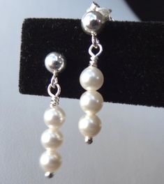 white pearls are hanging from silver earwires on a black velvet stand, with a pair of earrings in the foreground