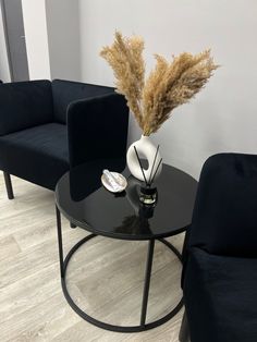 a black table with two chairs and a vase on it in front of a white wall