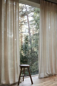 a wooden stool sitting in front of a window covered in white curtained drapes