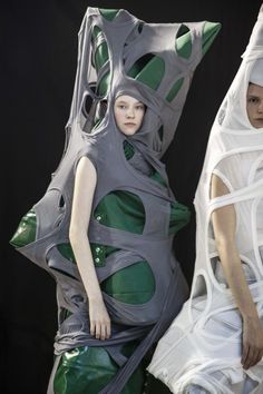 two models in white and green dresses with large headpieces on their heads, one wearing