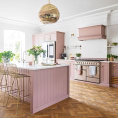 a kitchen with pink cabinets and wooden floors is pictured in this image, there are gold bar stools at the center of the island